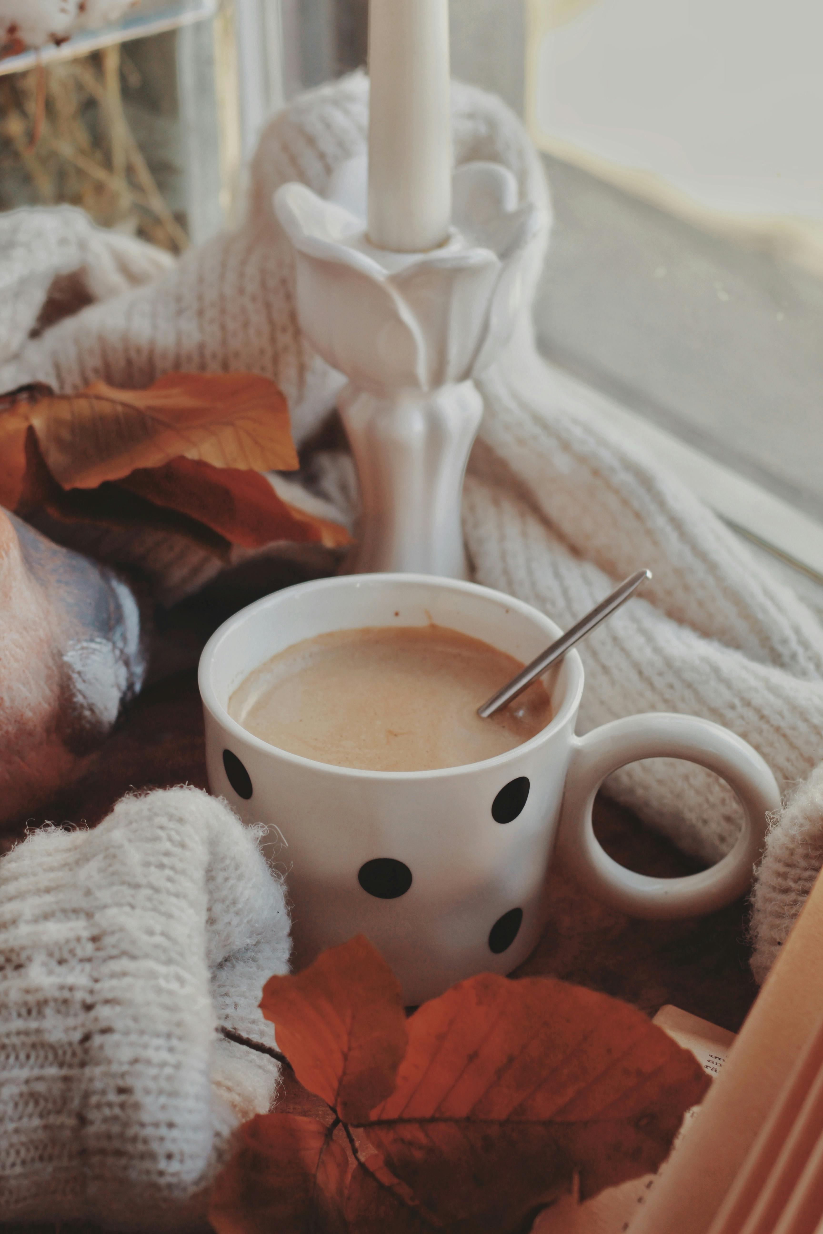 A warm cup of coffee surrounded by autumn leaves and a knitted blanket, evoking fall comforts.