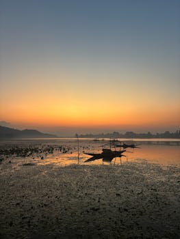 Peaceful sunrise over a lake with a solitary fishing boat and calm waters.