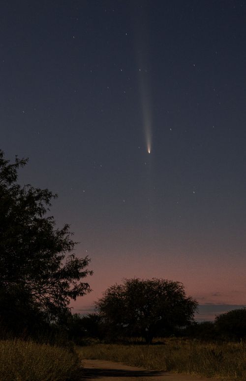 Free A serene nighttime view of a comet streaking across a star-filled sky above a tranquil landscape. Stock Photo