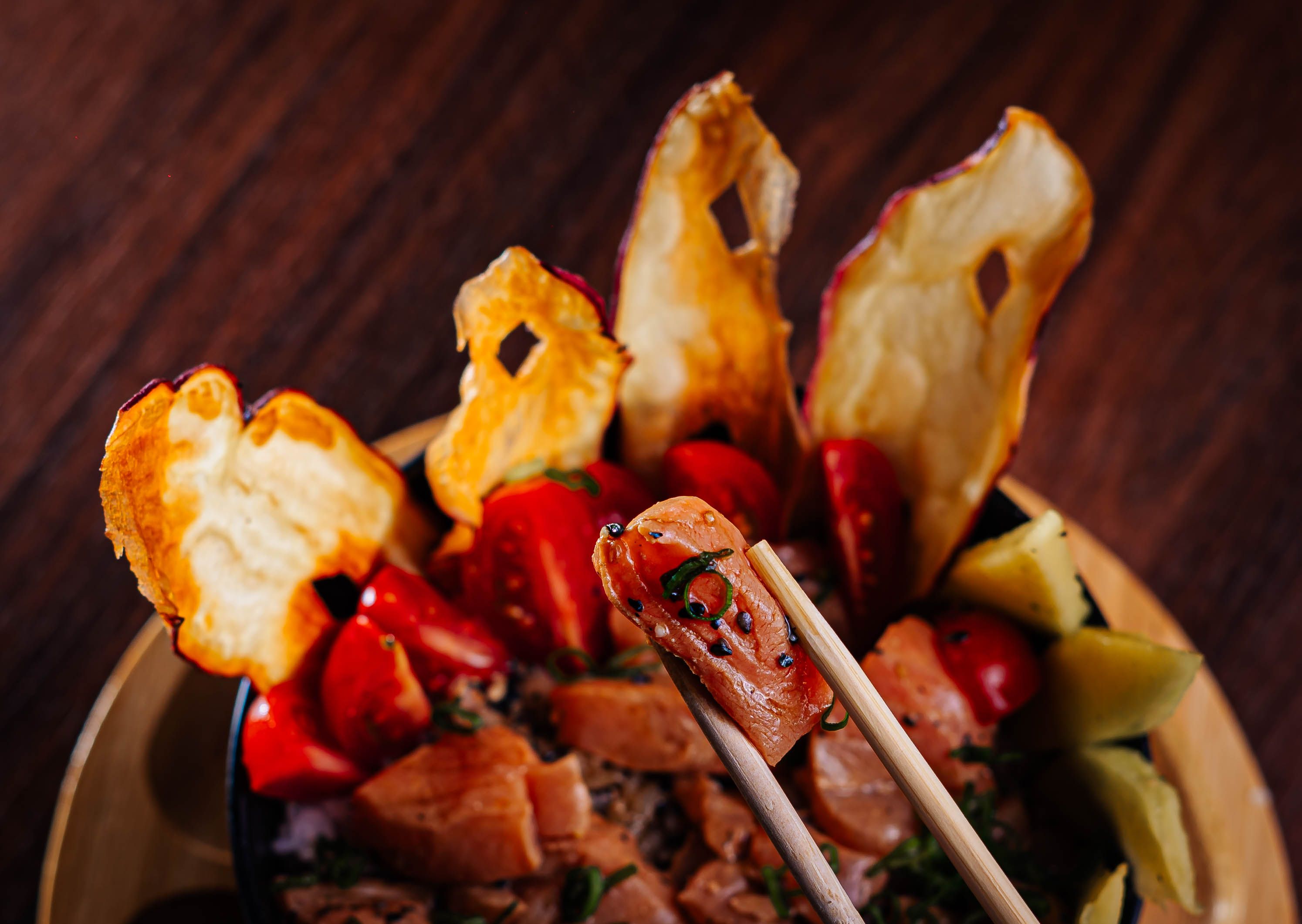 Close-up of a colorful salmon poke bowl with chopsticks, showcasing vibrant ingredients like dried fruit and vegetables.