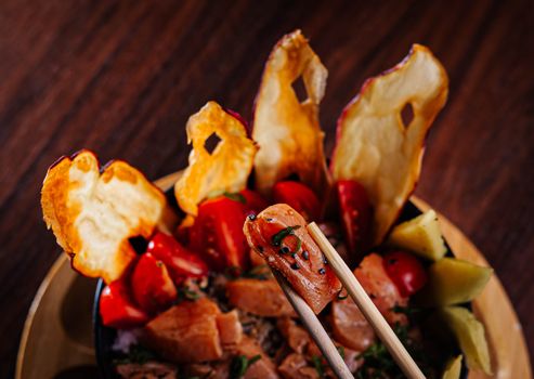 Close-up of a colorful salmon poke bowl with chopsticks, showcasing vibrant ingredients like dried fruit and vegetables.