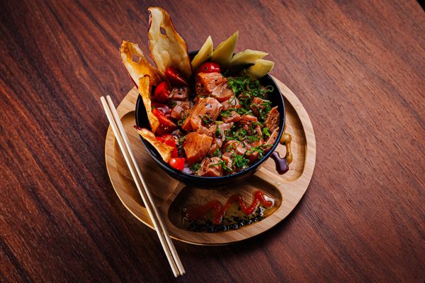 Salmon poke bowl with chopsticks on a wooden table — photo by pedro furtado on Pexels