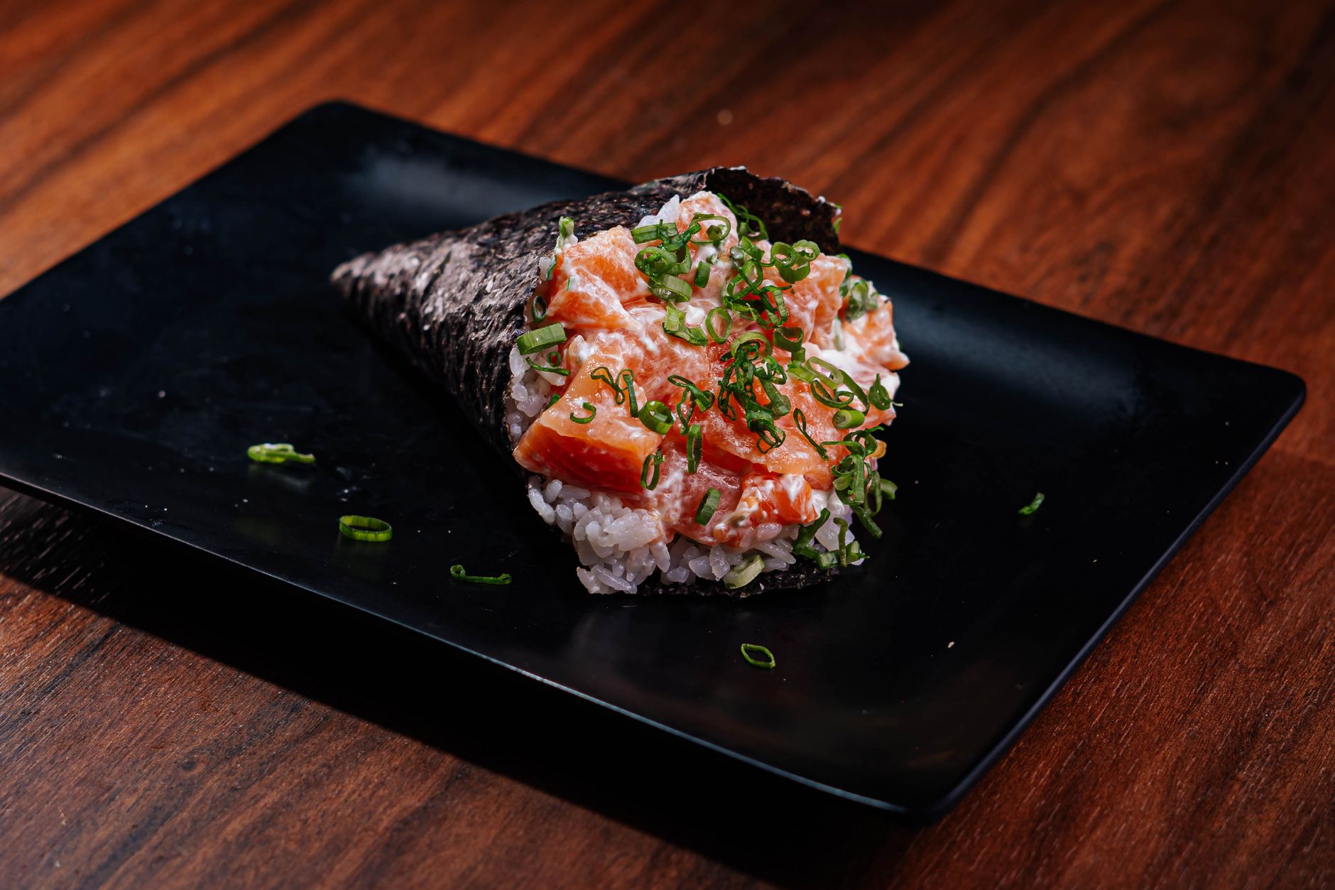 Sushi hand rolls freshly made on a wooden tray with dipping sauce on the side
