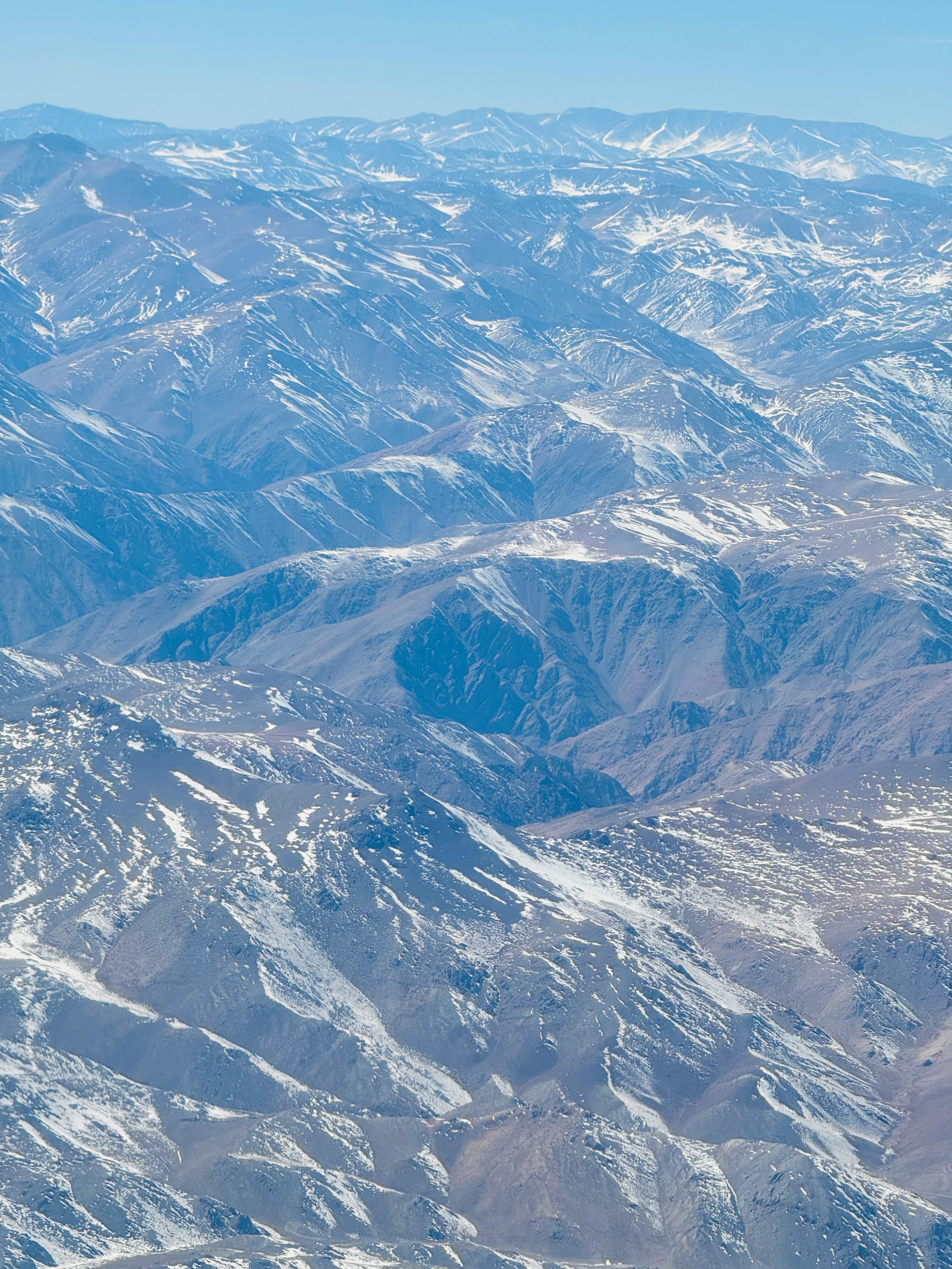Expansive aerial view of a snow-capped mountain range under a clear blue sky. Ideal for adventure themes.