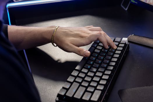 Close-up of a hand typing on a mechanical keyboard with illuminated keys in a dimly lit room.