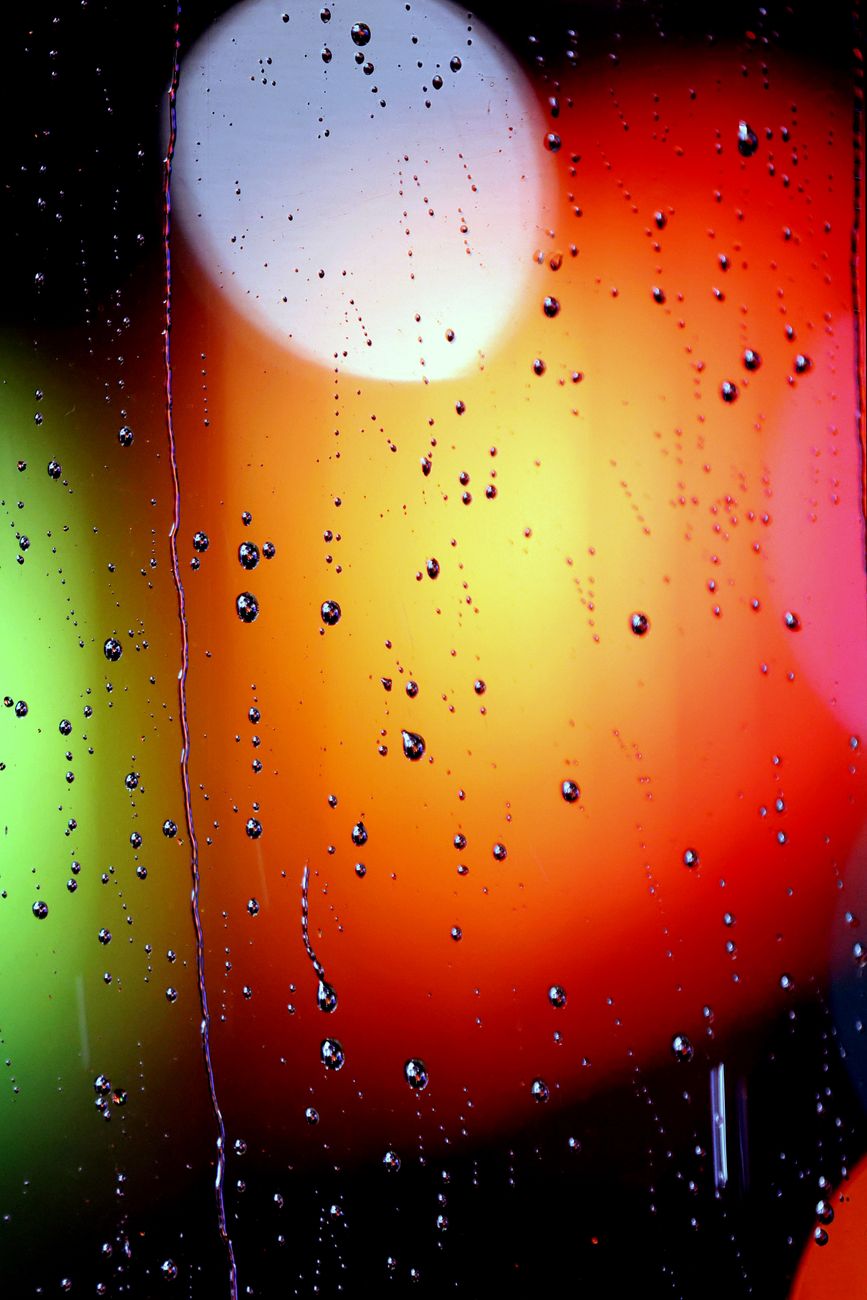 Raindrops on glass with colorful blurred lights creating a moody bokeh effect.