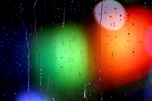 Vibrant raindrops on glass create a mesmerizing abstract pattern with colorful bokeh lights.