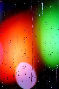 Abstract view through a rain-soaked window with vibrant bokeh lights in the background.
