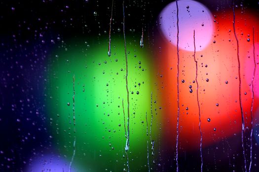Captivating rain droplets on glass with vibrant green and red bokeh background.