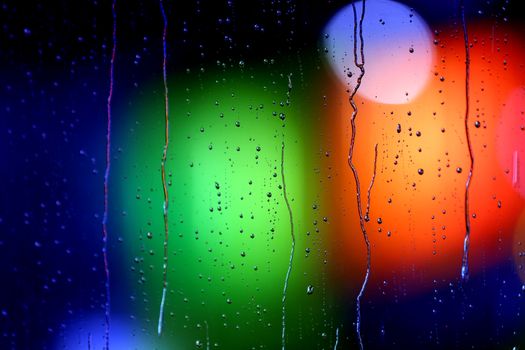 Vibrant raindrops on glass with a blurred urban bokeh light background.