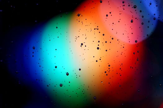 Vivid abstract image with rainbow colors and water droplets on glass.