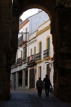 Silhouetted couple strolls through an ancient archway in a picturesque Spanish street.