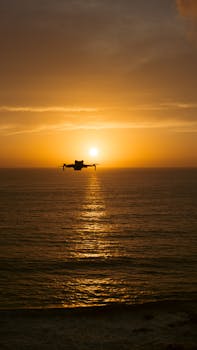 Silhouette of a drone flying over the ocean during a vibrant sunset, creating a serene scene.