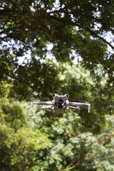 A drone hovers amid lush green trees, showcasing technology in nature.
