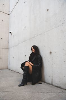 Stylish woman in black outfit leaning against a modern concrete wall in Ottawa.