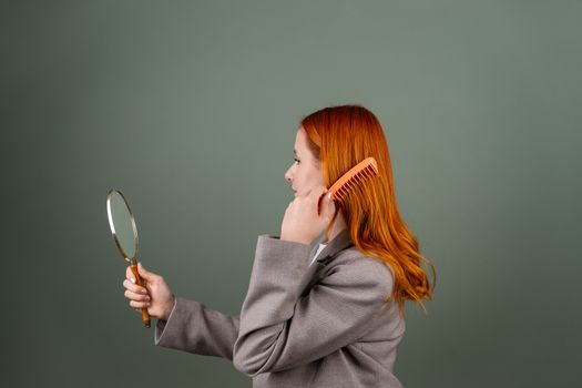 Side profile of a woman combing her hair and looking in a handheld mirror.