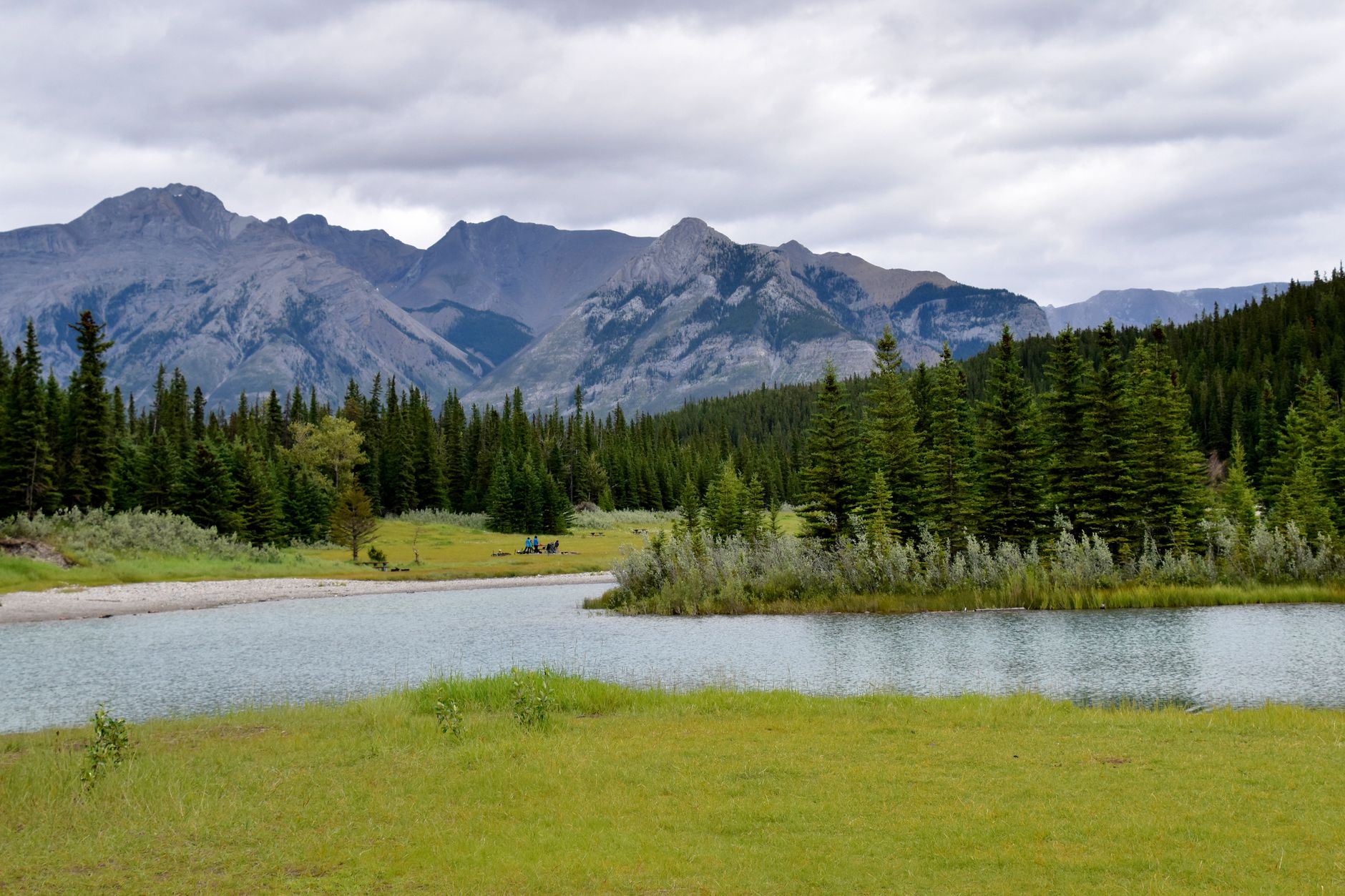 Serene landscape featuring mountains, a calm lake, and lush green conifers.