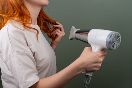 Woman blow drying her vibrant red hair with a modern blow dryer, showcasing hair styling technique.