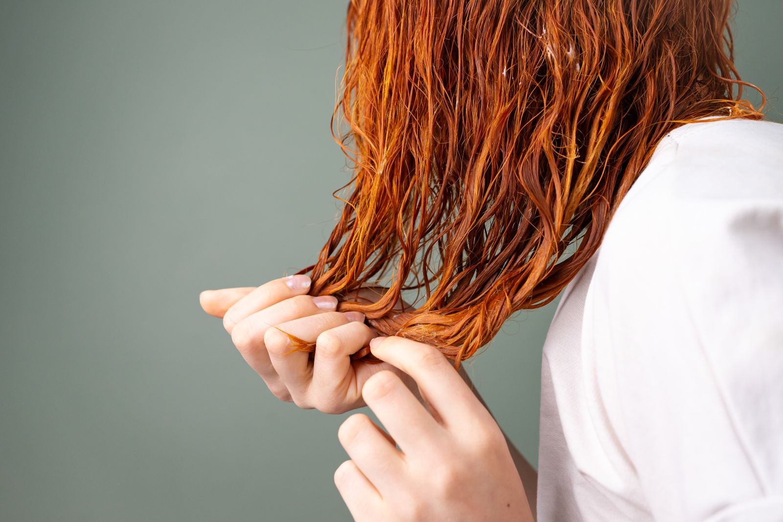 Hands gently separating strands of wet auburn hair against a muted neutral background