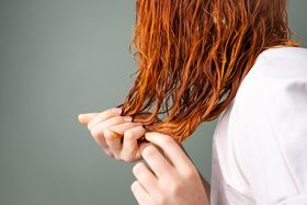 Hands gently separating strands of wet auburn hair against a muted neutral background