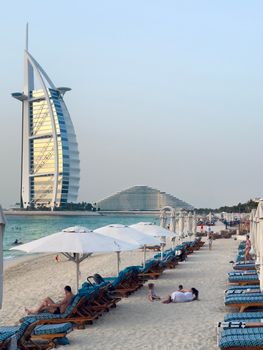 Scenic beach view with Burj Al Arab in Dubai, featuring people relaxing on sun loungers.