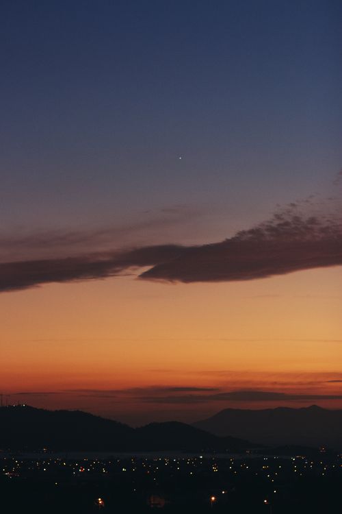 Free Stunning twilight scene with silhouetted hills and sparkling city lights under a colorful sky. Stock Photo