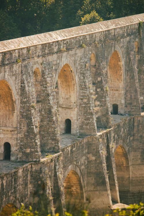 Free Close-up view of an ancient stone aqueduct with arches, bathed in warm sunlight. Stock Photo