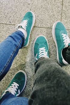 Three pairs of teal sneakers on a granite pavement in Gwangju, South Korea, showcasing casual fashion.