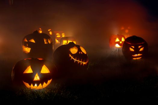 Eerie glowing jack-o'-lanterns in a foggy outdoor setting, perfect for Halloween themes.
