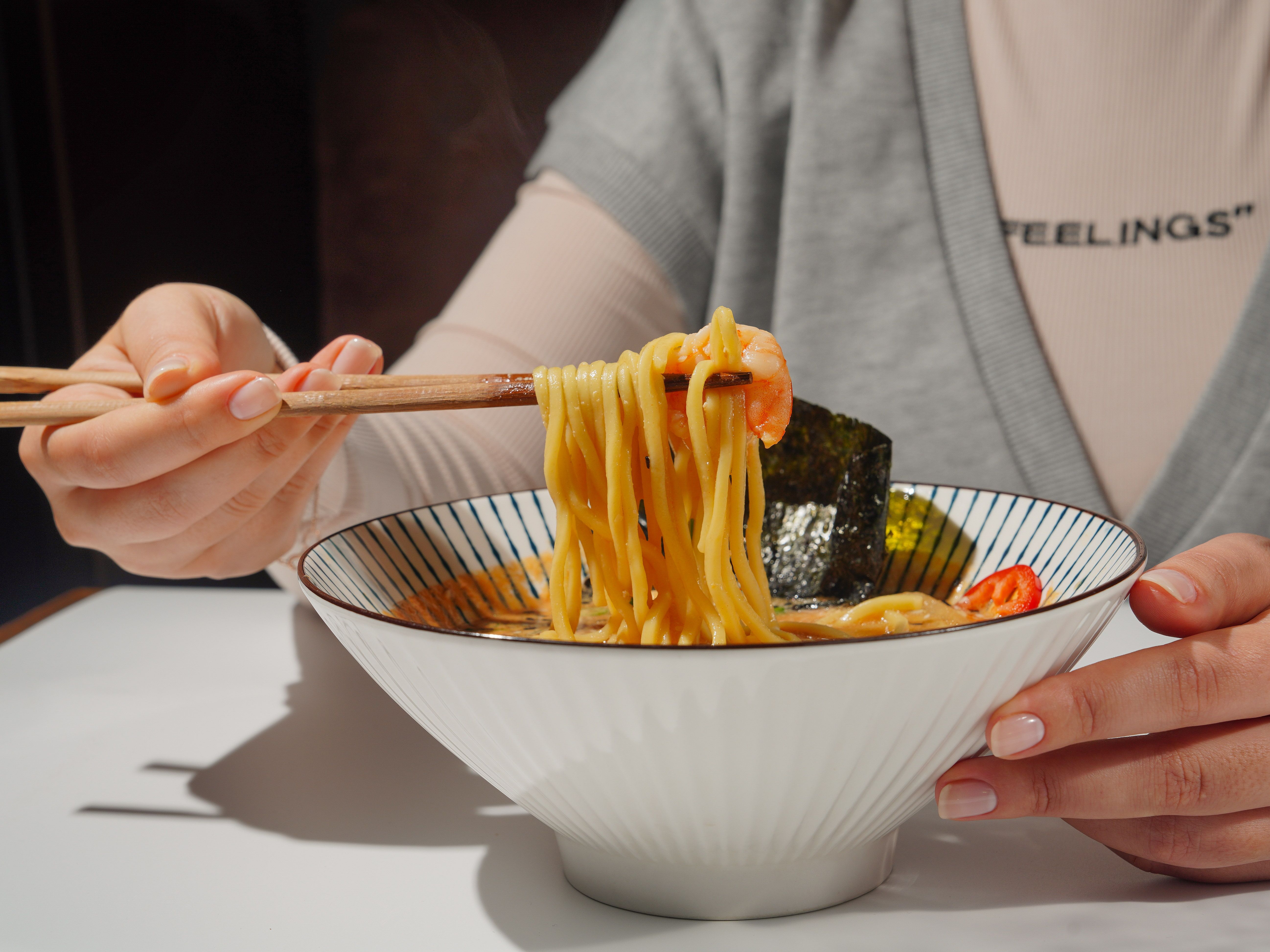 Close-up of a person eating ramen with chopsticks, highlighting the noodles and shrimp.