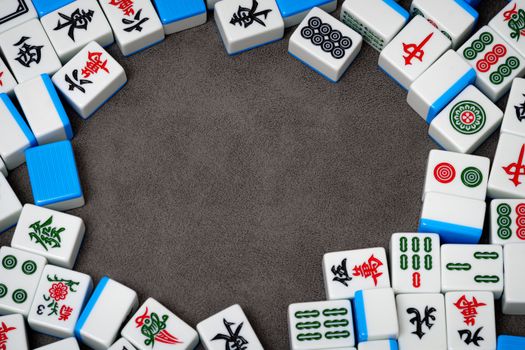Close-up of scattered Mahjong tiles with intricate designs on a textured gray background.