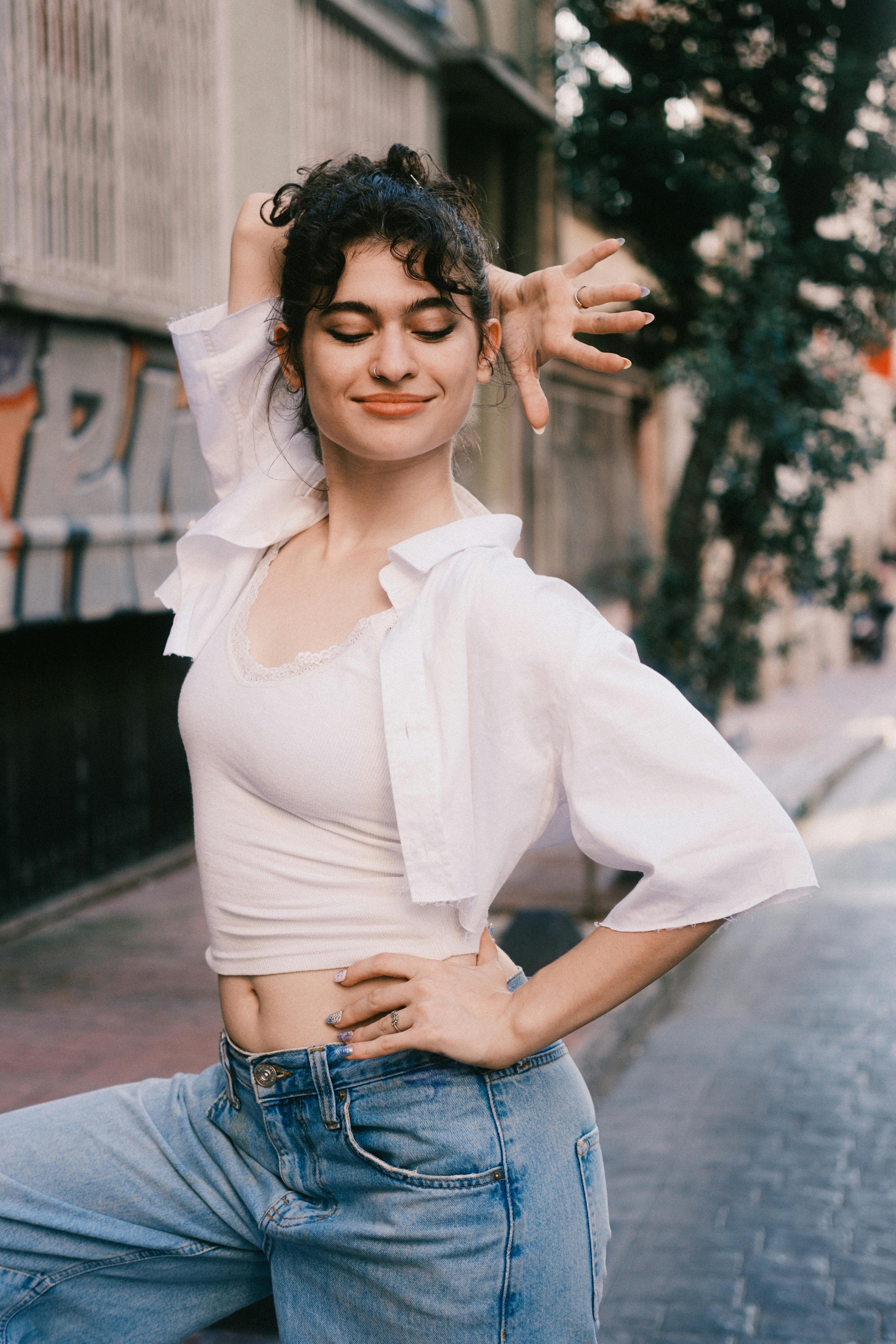 Smiling young woman in casual attire striking a confident pose on an urban street.