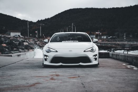 White sports car parked on a coastal road with an overcast sky background, exuding a cool and dramatic vibe.