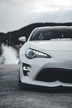Close-up of a white sports car parked on a scenic road with a mountainous backdrop.