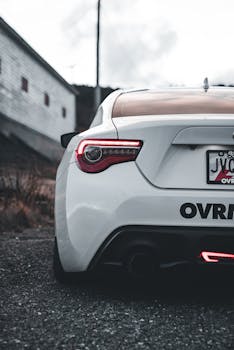 Close-up view of a modern white sports car with glowing tail lights on a moody outdoor scene.