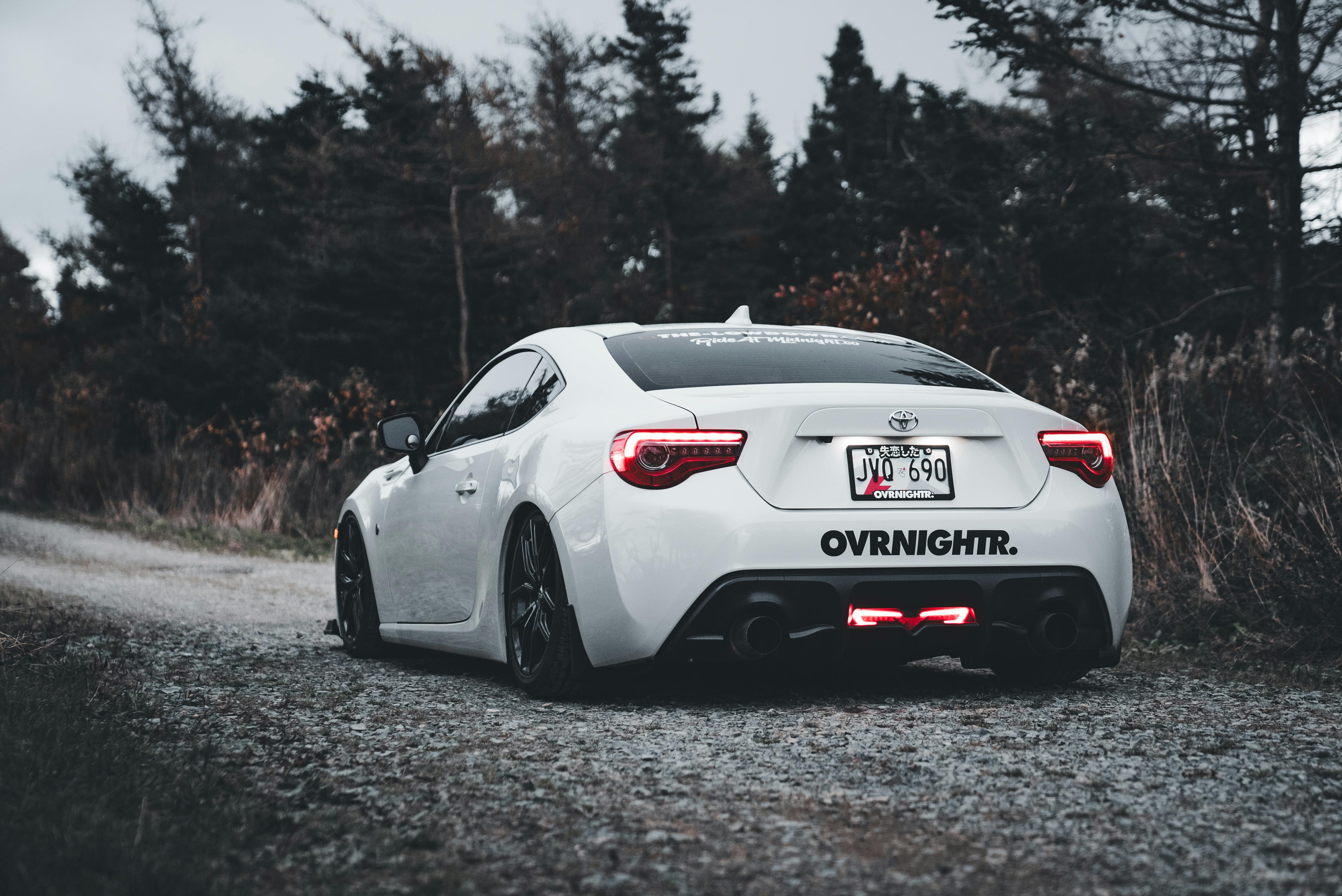 White sporty car parked on a quiet scenic forest road, showcasing sleek design and quiet surroundings.