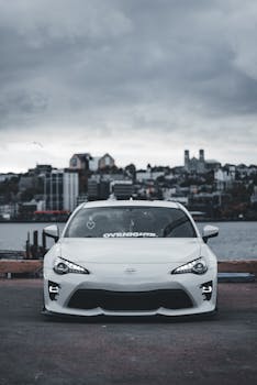 White car with urban skyline backdrop under a cloudy sky, emphasizing modern design and city living.