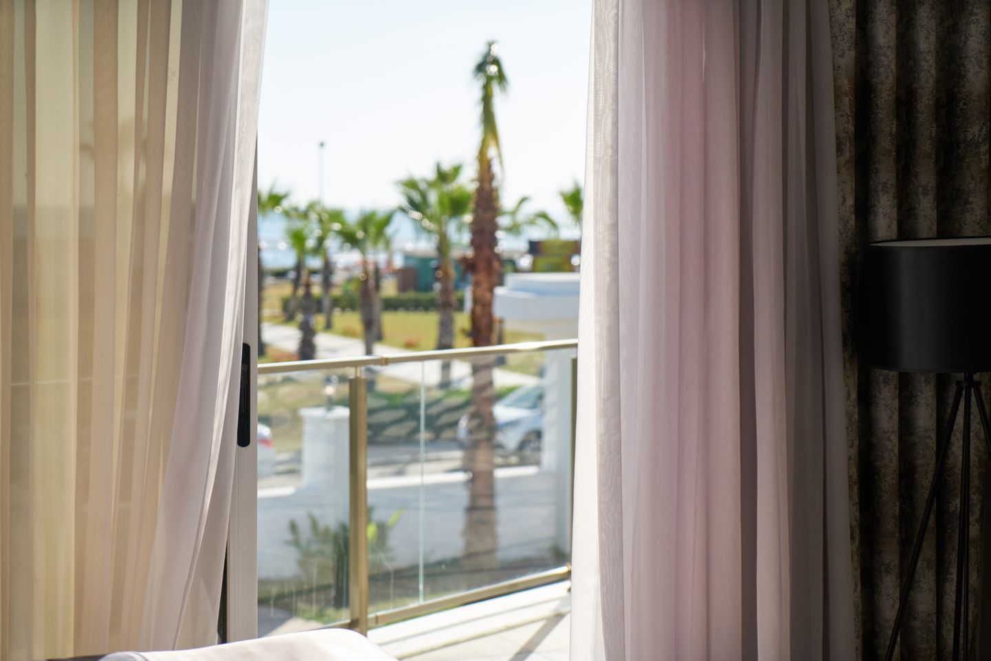 Hotel room balcony view with palm trees visible through floor-to-ceiling windows, bright daylight, Los Angeles