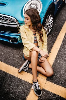 阳光明媚的日子里，一位穿着休闲装的年轻女子坐在一辆蓝色汽车旁