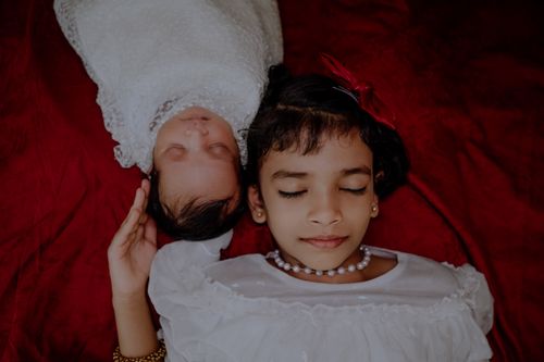 Free Close-up of a baby and child resting peacefully on red fabric, wearing white. Stock Photo