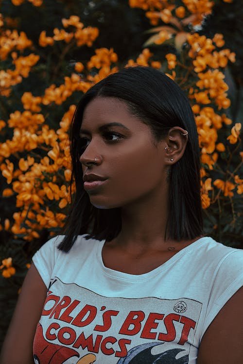 Photo of Woman in White T-shirt Posing While Looking Away With Yellow Flowers in the Background