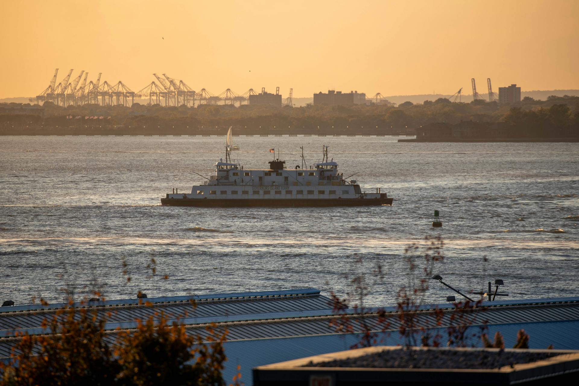 Serene sunset over New York Harbor with a ferry boat and industrial skyline.