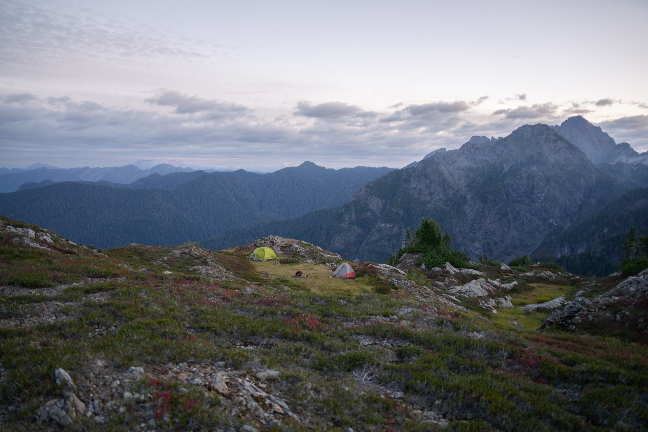 Backcountry campsite with tents nestled near mountains in Washington state wilderness at sunrise Backcountry campsite with tents nestled near mountains in Washington state wilderness at sunrise