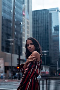Woman in striped dress posing confidently in bustling city environment with skyscrapers in background.