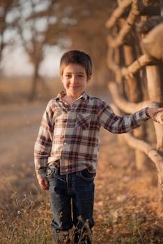Young boy smiling by a rustic fence in a sunlit field during golden hour.