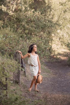 A young girl walks in a sunny woodland holding a hat, radiating a serene summer vibe.