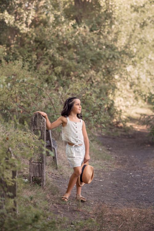 Free A young girl walks in a sunny woodland holding a hat, radiating a serene summer vibe. Stock Photo