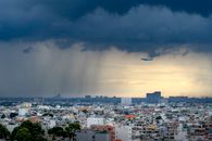 Dramatic view of a plane flying over a city during a storm with heavy clouds and rain.