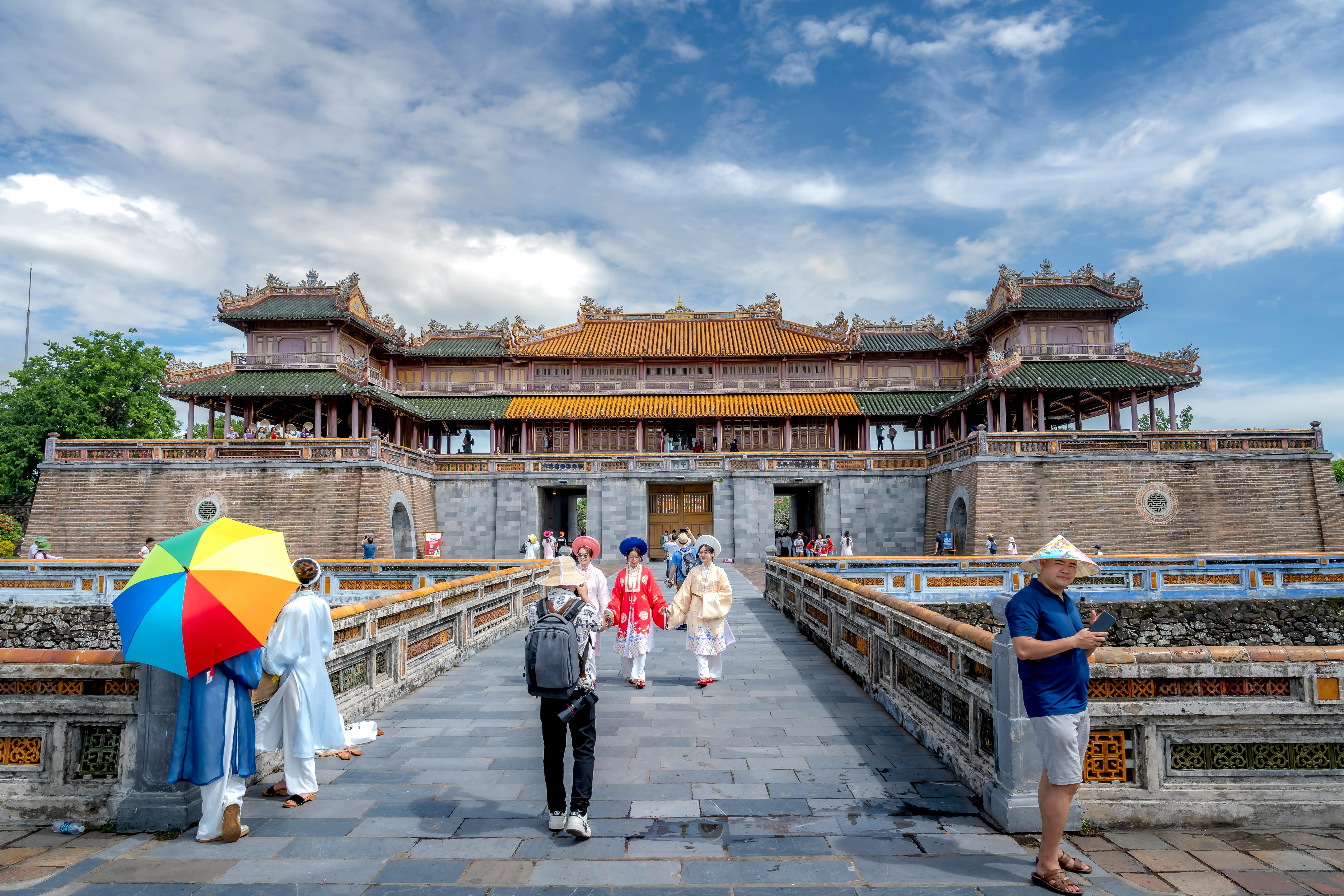 Tourists explore the historic Hue Imperial Citadel under a clear blue sky.