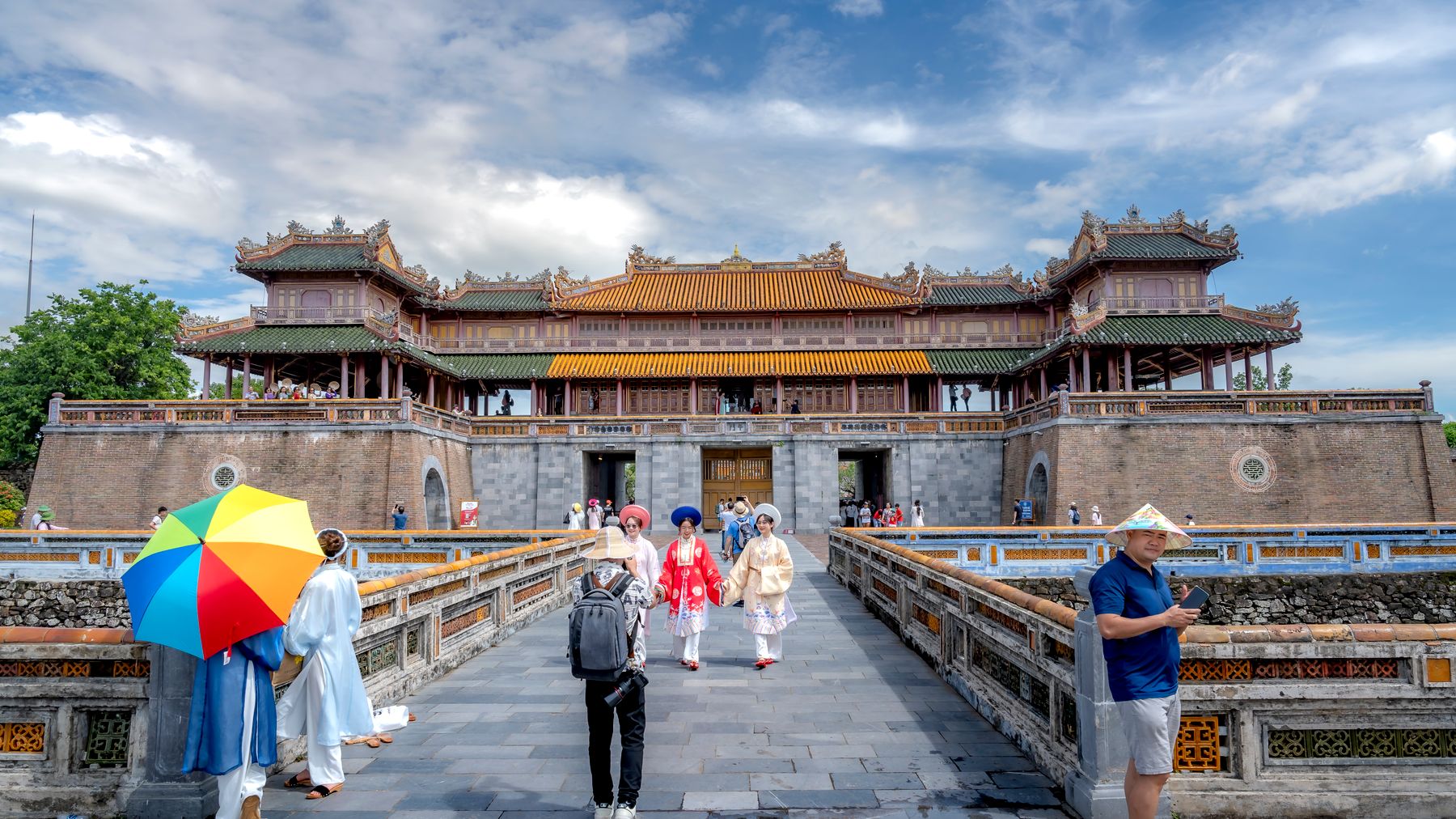 Tourists explore the historic Hue Imperial Citadel under a clear blue sky.